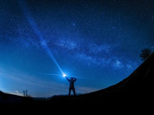 A guide with a flashlight in the night with stars.